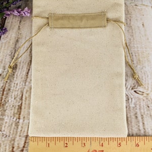 Puede incluir: Una bolsa de cord&oacute;n blanco liso con una solapa de tela beige y un cierre de cord&oacute;n. La bolsa mide 15 cm de ancho y 20 cm de alto.