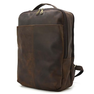 May include: A brown leather backpack with a top handle and a front pocket. The backpack has a zipper closure and brass-colored hardware. The leather has a distressed look.