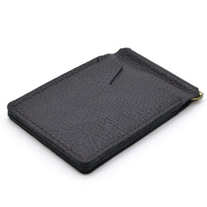Puede incluir: Una cartera con clip para dinero de cuero marr&oacute;n oscuro con una superficie de grano texturizado, bordes cosidos y una ranura vertical para tarjetas en la parte frontal. Un clip de resorte dorado est&aacute; sujeto al borde superior para asegurar billetes.