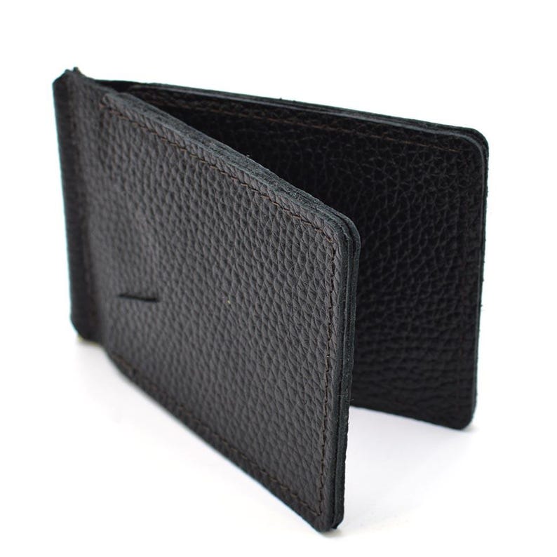 Puede incluir: Una cartera con clip para dinero de cuero negro que presenta una superficie texturizada y granulada. La cartera est&aacute; construida con un mecanismo de clip met&aacute;lico con bisagras integrado en el lomo, dise&ntilde;ado para sujetar billetes entre dos paneles.
