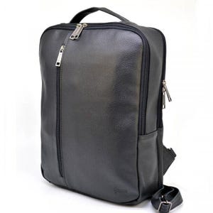 May include: Black leather backpack with a rectangular design. It has a top handle, a vertical front zip, and a smaller side zip. The bag has a textured finish and silver-coloured hardware. Includes adjustable shoulder straps.