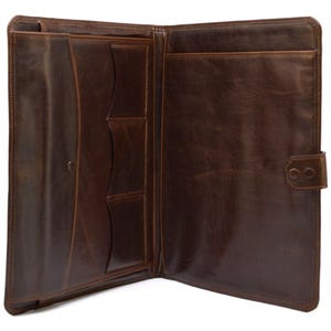 May include: Open brown leather portfolio with multiple pockets and a snap closure. The interior features various compartments for documents and cards. The leather has a distressed finish, giving it a vintage look. The portfolio is designed to hold papers and other items.