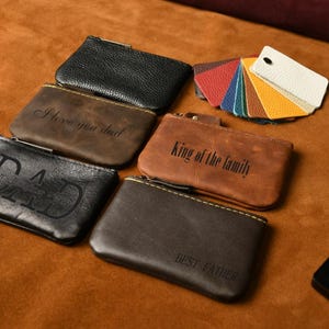 May include: A collection of rectangular leather pouches in black, brown, and tan, featuring engraved text including "I love you dad," "King of the family," "DAD," and "BEST FATHER," accompanied by a fan of small, multi-colored leather swatches.