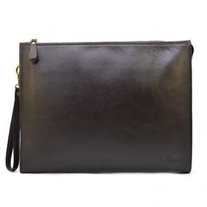 May include: A dark brown leather clutch with a wrist strap and a gold-colored zipper. The rectangular bag has a smooth texture and a small logo on the bottom right corner. The wrist strap is attached with a gold-colored clasp.