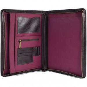 May include: Open black leather portfolio with a burgundy interior. The portfolio has multiple pockets, including card slots, a zippered pocket, and a large document sleeve. A brass zip secures the portfolio.
