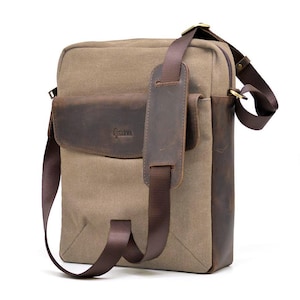 Op de afbeelding: Een beige canvas messenger bag met bruine lederen accenten. De tas heeft een leren flap met de merknaam "TARWA", een bruine verstelbare schouderriem en een zijvak. De tas is rechthoekig en heeft een ritssluiting.