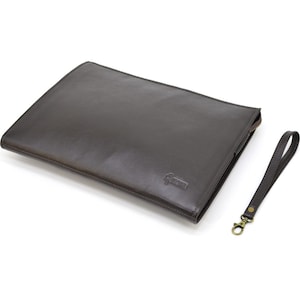 May include: A dark brown leather document case with a matching wrist strap. The case has a rectangular shape with a subtle embossed logo in the lower right corner. The wrist strap is attached with a brass-colored clasp.