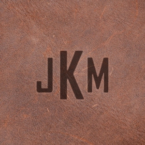 a close-up of a brown leather surface with the initials "JKM" prominently displayed in the center.