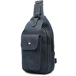 Pode incluir: Uma bolsa de couro azul com uma bolsa frontal e um compartimento principal com zíper. A bolsa tem uma alça de ombro com uma fivela de metal e um pequeno bolso com fecho de botão. A bolsa é feita de couro.