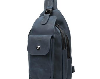 May include: A blue leather sling bag with a front pocket and a zippered main compartment. The bag has a shoulder strap with a metal buckle and a small pocket with a button closure. The bag is made of a distressed leather material.