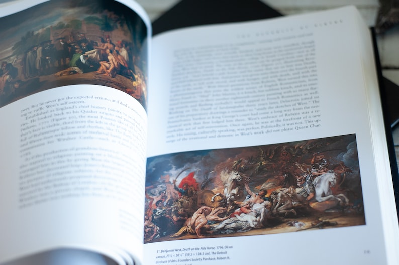 May include: Open book with a detailed painting of a battle scene, featuring figures on horseback and fallen soldiers. The artwork is vibrant with reds, whites, and browns. Text on the page describes the painting and its artist.