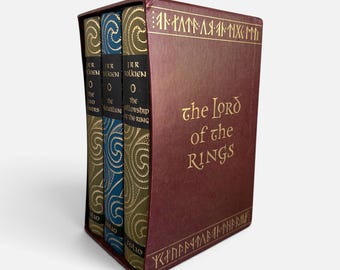 May include: A three-volume book set of The Lord of the Rings housed in a dark red slipcase with gold lettering and runic symbols. The spines are colored dark red, blue, and green, each featuring intricate gold patterns and the author's name.