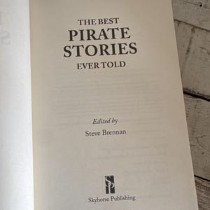 Pu&ograve; includere: Libro aperto con il titolo "THE BEST PIRATE STORIES EVER TOLD" in grandi lettere nere. Curato da Steve Brennan e pubblicato da Skyhorse Publishing. Le pagine sono color crema.
