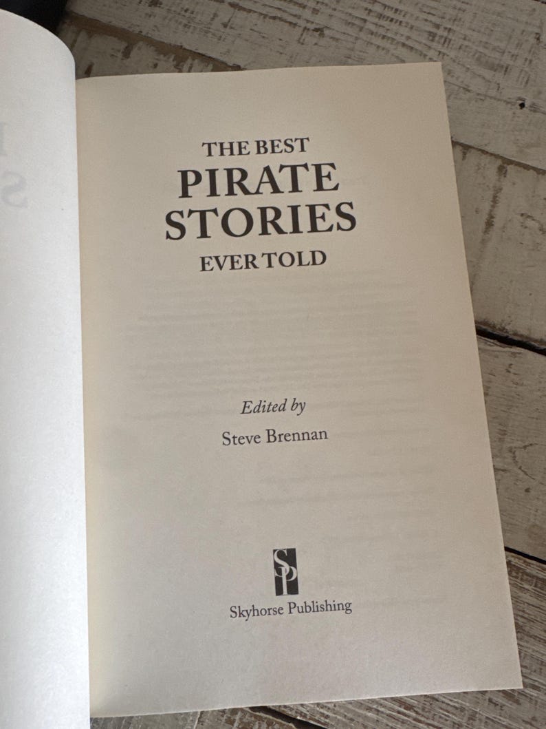 Pu&ograve; includere: Libro aperto con il titolo "THE BEST PIRATE STORIES EVER TOLD" in grandi lettere nere. Curato da Steve Brennan e pubblicato da Skyhorse Publishing. Le pagine sono color crema.