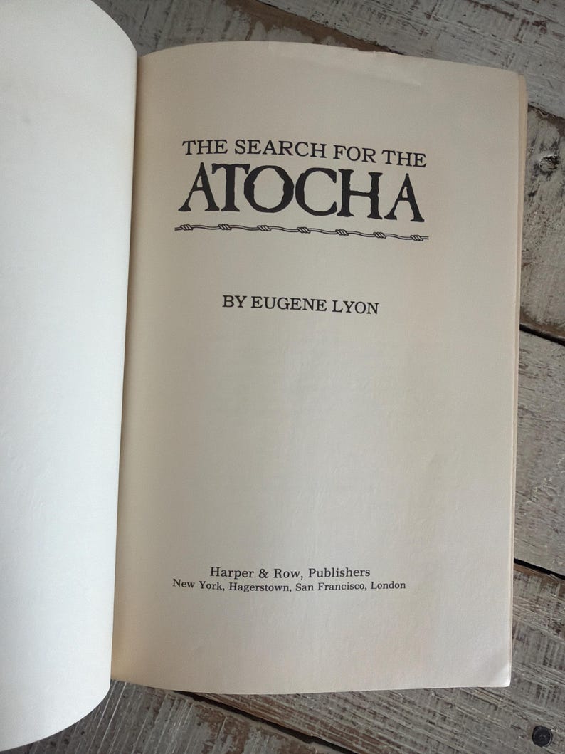 May include: An open book displaying the title "THE SEARCH FOR THE ATOCHA" in black lettering. The author's name, Eugene Lyon, is below the title. The publisher's name, Harper & Row, is at the bottom.