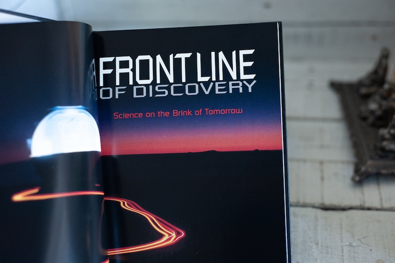 May include: Open book with the title "FRONT LINE OF DISCOVERY" in white, and the subtitle "Science on the Brink of Tomorrow" in red. The background shows a dark landscape with a sunset.