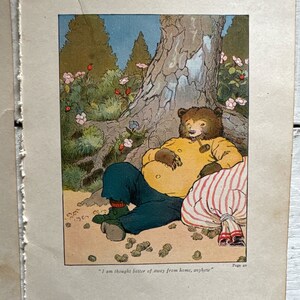 May include: A cartoon illustration of a bear wearing a yellow shirt and blue pants sitting under a tree with a striped bag. The bear is holding a pipe in its mouth and has a thoughtful expression on its face. The text "I am thought better of away from home, anyhow" is printed below the image.