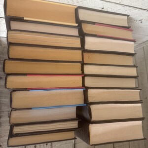 May include: A stack of hardcover books with tan pages and dark brown spines. The books are arranged in two columns, with the spines facing outward. Some books have colored page edges, including red and blue.