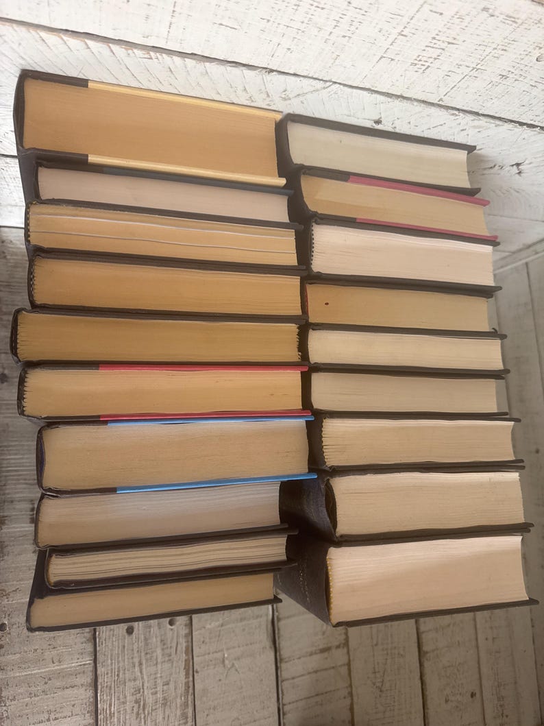 May include: A stack of hardcover books with tan pages and dark brown spines. The books are arranged in two columns, with the spines facing outward. Some books have colored page edges, including red and blue.