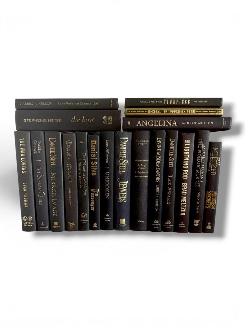 May include: A collection of hardcover books with dark covers, arranged in stacks and rows. Titles and authors are visible, with gold lettering on some spines. The books vary in size and include titles like "The Host" and "Angelina".