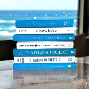 May include: A stack of seven blue and white paperback books with titles visible. The books are stacked on a white surface. The titles of the books are "Everything in Its Place", "elsewhere", "extravagant", "The Warden's Daughter", "The Athena Project", "Talking to Robots", and "Ill Met in the Arena".