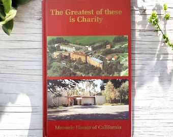 May include: A red hardcover book with the title "The Greatest of these is Charity" and the subtitle "Masonic Homes of California". The cover features two aerial photographs of buildings.