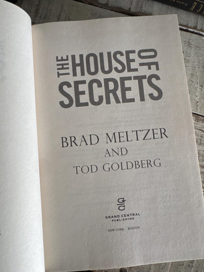 May include: Open book with the title "THE HOUSE OF SECRETS" in large, gray letters. The authors' names, Brad Meltzer and Tod Goldberg, are below. The Grand Central Publishing logo and city names are at the bottom.
