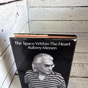 May include: A black and white book cover with the title "The Space Within The Heart" by Aubrey Menen. The cover features a black and white photo of a man with grey hair and glasses.