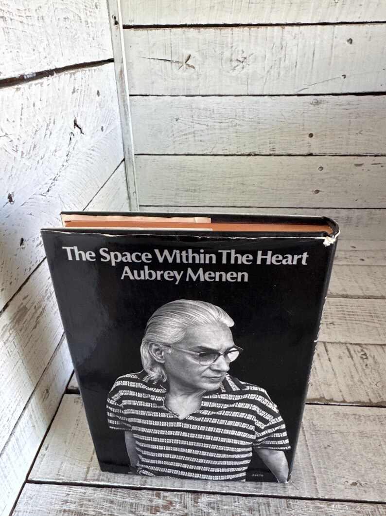 May include: A black and white book cover with the title "The Space Within The Heart" by Aubrey Menen. The cover features a black and white photo of a man with grey hair and glasses.