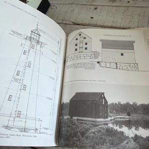 May include: An open book displaying black and white architectural drawings and a photograph of historical structures. The left page shows a technical diagram of a lighthouse in Sandy Hook, New Jersey. The right page features the Van Wyck-Lefferts Tide Mill.