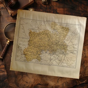 May include: An antique map of Middlesex, England, with a detailed depiction of the region's roads and towns. The map is aged with a yellowed paper appearance, and is accompanied by a magnifying glass and other vintage items.