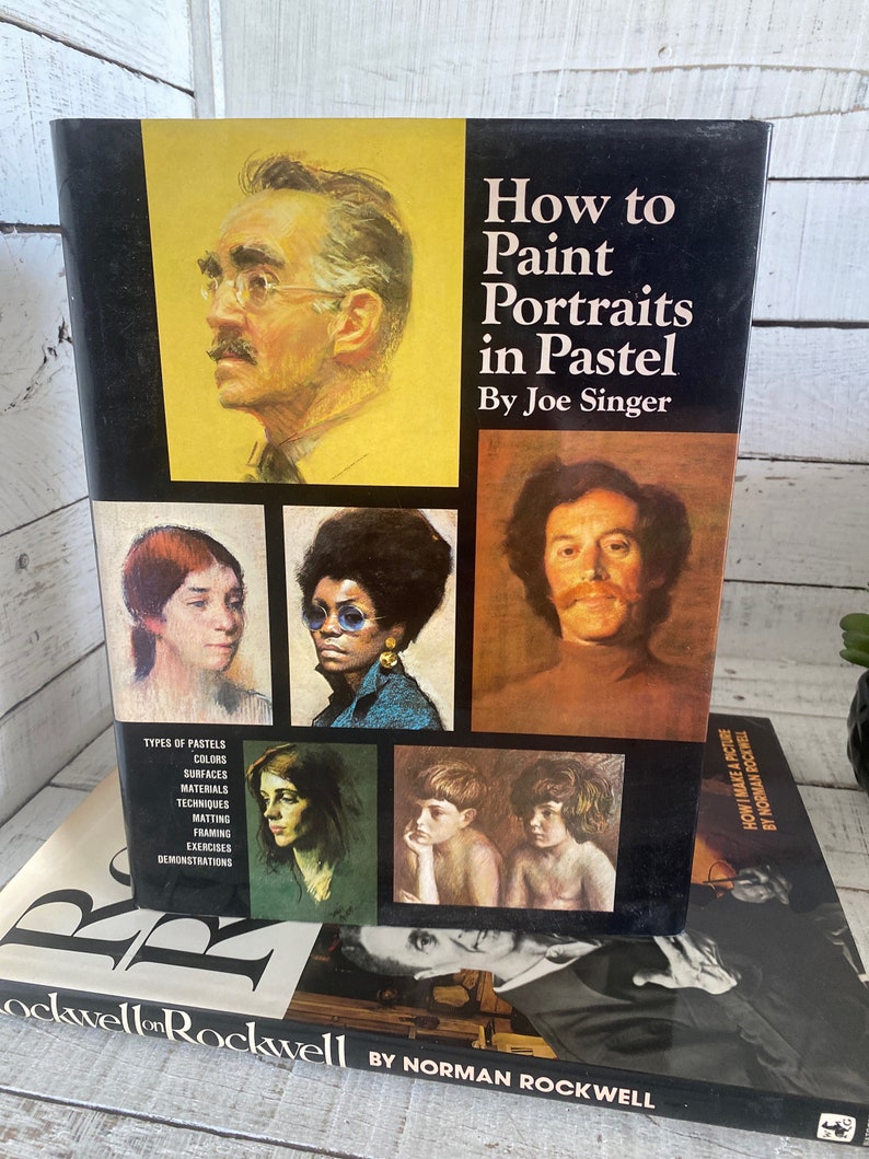 K&ouml;nnte beinhalten: Ein Buch mit dem Titel "Wie man Portr&auml;ts in Pastell malt" von Joe Singer. Der Umschlag zeigt eine Auswahl an Pastellportr&auml;ts von Menschen, darunter ein Mann mit Schnurrbart, eine Frau mit Brille und ein kleiner Junge.