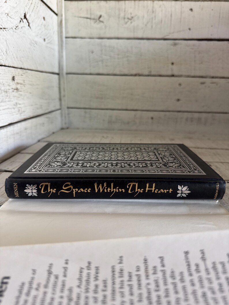 May include: A black hardback book with a silver and black patterned cover. The title "The Space Within The Heart" is written in gold lettering on the spine.