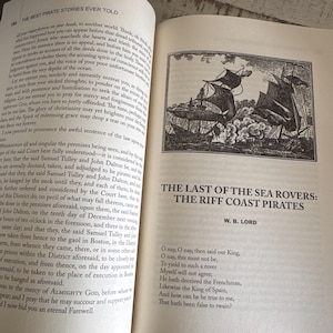 Pu&ograve; includere: Libro aperto con testo e un'illustrazione di velieri. Il titolo recita "The Last of the Sea Rovers: The Riff Coast Pirates" di W.B. Lord. La pagina contiene anche una poesia.