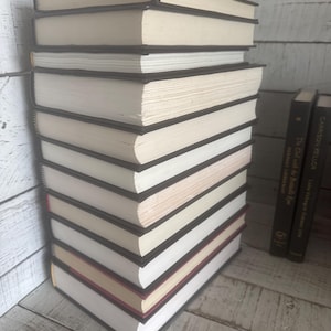 May include: A stack of hardcover books with black spines and off-white pages. The books are neatly arranged, with some showing red and gold accents on their edges. The background features a white wooden surface.