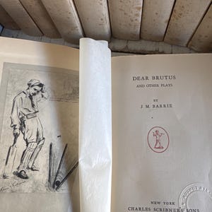 Puede incluir: Libro abierto titulado "DEAR BRUTUS AND OTHER PLAYS" de J.M. Barrie. La portada es blanquecina con texto negro. Un dibujo de un jugador de cr&iacute;quet est&aacute; en la p&aacute;gina izquierda. Publicado por Charles Scribner's Sons, Nueva York, MCMXXXI.