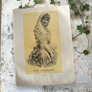 May include: A black and white portrait of Sarah Bernhardt, a famous French actress, wearing a lace veil and dress. The image is printed on a yellowed page with the text "SARA BERNHARDT." and "Plate 149."