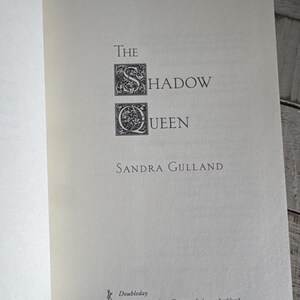 May include: Open book page with the title "The Shadow Queen" by Sandra Gulland. The title is in a serif font with decorative capital letters. The publisher, Doubleday, is listed at the bottom, with locations including New York and London.