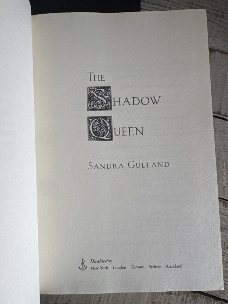 May include: Open book page with the title "The Shadow Queen" by Sandra Gulland. The title is in a serif font with decorative capital letters. The publisher, Doubleday, is listed at the bottom, with locations including New York and London.