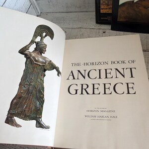 May include: An open hardcover book titled The Horizon Book of Ancient Greece by William Harlan Hale. The left page features a color illustration of a bronze statue of a figure in a helmet and robe, while the right page displays the title text.