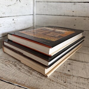 May include: A stack of three hardcover books with white pages. The top book features a dark cover with a rectangular image of a house and text that reads "CAROLE RIFKIND" and "A FIELD GUIDE TO AMERICAN ARCHITECTURE". The middle and bottom books have plain covers.