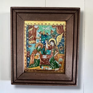May include: A framed, vintage religious painting with a dark brown wooden frame. The artwork depicts two figures, one with a halo, in colorful robes. The background features floral and architectural elements. The painting is dated 1866.