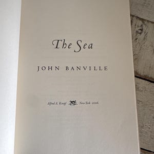 Pu&ograve; includere: Pagina di libro aperta con il titolo "The Sea" di John Banville. Il nome dell'editore, Alfred A. Knopf, e l'anno 2006 sono stampati sulla pagina. La pagina &egrave; di colore crema chiaro.