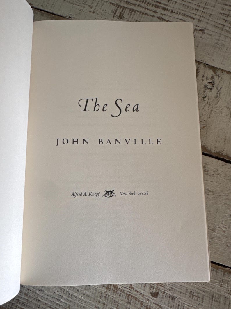 Pu&ograve; includere: Pagina di libro aperta con il titolo "The Sea" di John Banville. Il nome dell'editore, Alfred A. Knopf, e l'anno 2006 sono stampati sulla pagina. La pagina &egrave; di colore crema chiaro.