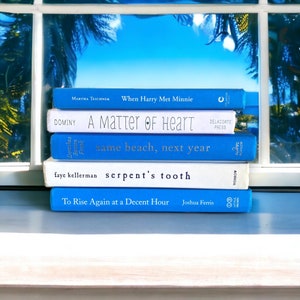 May include: A stack of five paperback books with blue and white covers. The titles of the books are "When Harry Met Minnie", "A Matter of Heart", "same beach, next year", "serpent's tooth", and "To Rise Again at a Decent Hour".
