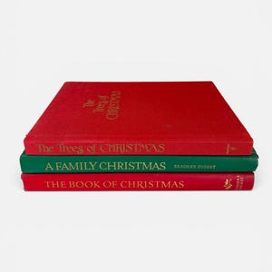 May include: A stack of three hardcover books with Christmas themes. The top book is red with gold text reading The Trees of Christmas. The middle book is green with white text reading A FAMILY CHRISTMAS READERS DIGEST. The bottom book is red with gold text reading THE BOOK OF CHRISTMAS.
