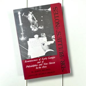 May include: A vintage book titled "DR. BULLIE'S NOTES" with a red spine and cover text. The cover features a black and white image of a desk with a candle, statue, and a person writing. The book's subtitle reads "Reminiscences of Early Georgia and of Philadelphia and New Haven In the 1800s."