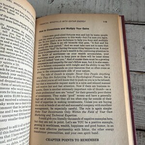 Puede incluir: Libro abierto con el t&iacute;tulo "Financial Windfalls with Ishtar Energy" sobre una superficie de madera. La p&aacute;gina muestra texto sobre la consolidaci&oacute;n y multiplicaci&oacute;n de ganancias. El libro tiene una cubierta roja.