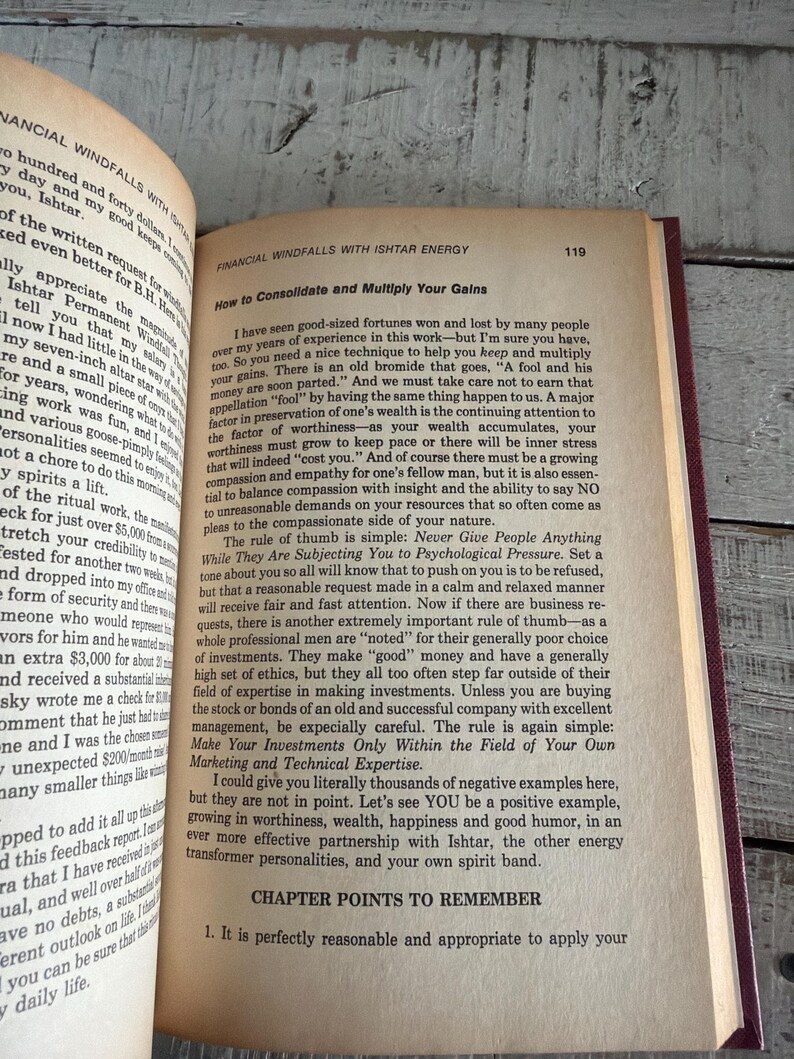 Puede incluir: Libro abierto con el t&iacute;tulo "Financial Windfalls with Ishtar Energy" sobre una superficie de madera. La p&aacute;gina muestra texto sobre la consolidaci&oacute;n y multiplicaci&oacute;n de ganancias. El libro tiene una cubierta roja.