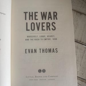 May include: Open book with the title "THE WAR LOVERS" in large, dark gray letters. Below, smaller text reads "ROOSEVELT, LODGE, HEARST, AND THE RUSH TO EMPIRE, 1898." The author's name, EVAN THOMAS, is also visible. The book is published by Little, Brown and Company.
